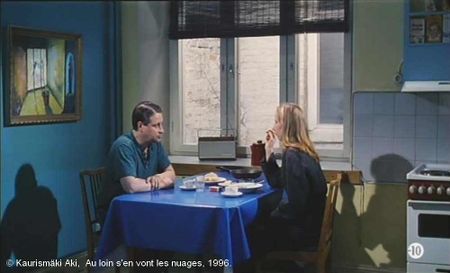 Au loin s'en vont les nuages de Kaurismäki Aki.   Photogramme - 5.   C'est le matin, le couple prend le petit déjeuner. Il faut noter la dominante bleue de la cuisine, les ombres portées du couple de part et d'autre de la table, et le tableau de peinture à gauche.