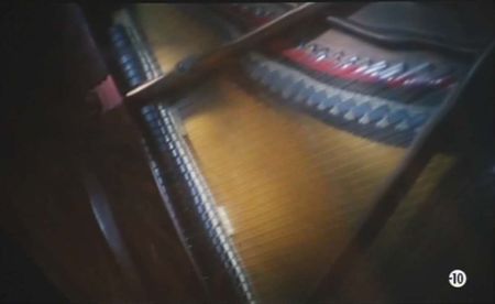 Au loin s'en vont les nuages de Kaurismäki Aki.   Photogramme - 1.  Gros plan de l'intérieur d'un piano à queue, plus précisément sur la table d'harmonie avec ses cordes et ses chevalets.